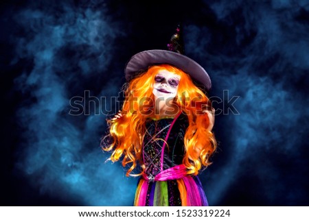 Beautiful girl in a witch costume on a dark background in smoke. Portrait of little girl in carnival costume of sorceress, background on halloween.
