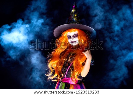 Beautiful girl in a witch costume on a dark background in smoke. Portrait of little girl in carnival costume of sorceress, background on halloween.