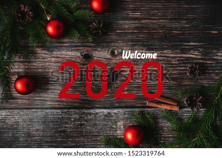 greeting card with red balls with tree branches on a wooden background and the inscription Welcome 2020
