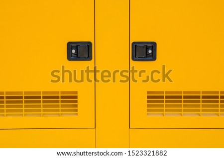 Front view panel of a new yellow outdoor electric current generator with two doors for emergency needs electric power supply. Minimalist symmetrical shapes urban background Royalty-Free Stock Photo #1523321882