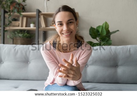 Smiling young woman blogger influencer sit on sofa looking at camera make video conference call recording vlog at home, happy girl vlogger do online chat shooting blog at home, portrait, webcam view Royalty-Free Stock Photo #1523325032