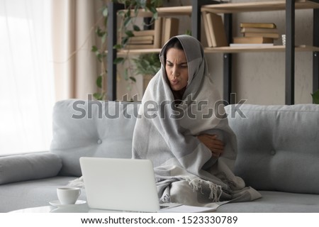 Sick ill young woman feel cold covered with blanket sit on sofa watching movie on laptop, annoyed girl shiver freezing warming at home wrapped with plaid, no central heating problem and flu concept Royalty-Free Stock Photo #1523330789
