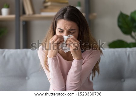 Allergic ill young woman sit on sofa holding tissue blowing running nose got fever caught cold sneezing in handkerchief, sick girl having influenza virus flu symptom coughing at home, allergy concept Royalty-Free Stock Photo #1523330798