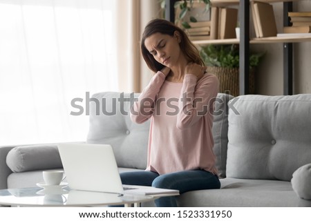 Tired young woman touch stiff neck feeling hurt joint back pain rubbing massaging tensed muscles suffer from fibromyalgia ache after long computer work study in incorrect posture sit on sofa at home  Royalty-Free Stock Photo #1523331950