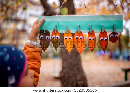 Seven autumn leaves with toy eyes from green to red on the clothespin over beautiful fall background, funny autumnal time concept, outdoor