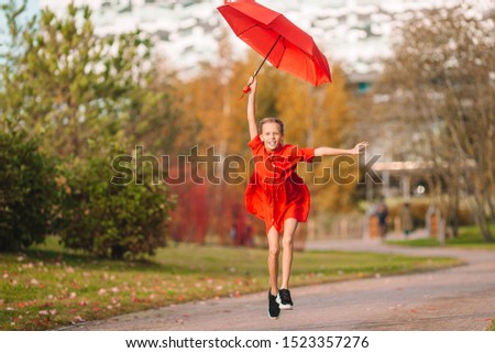 Happy adorable kid with red umbrella on an autumn walk at warm day