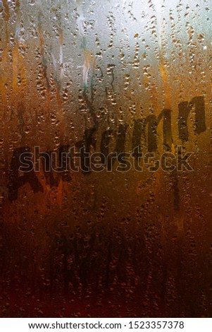 Word Autumn written on wet window with drops of water. Autumn, fall concept, moody picture with text to use at design