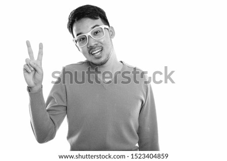 Studio shot of young happy Asian man smiling and giving peace sign