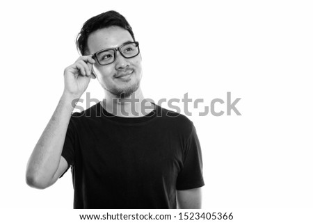 Studio shot of young Asian man holding eyeglasses while thinking