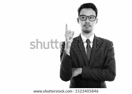 Studio shot of young Asian businessman pointing finger up while thinking