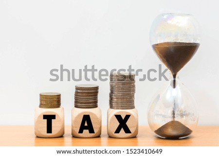 Wood cube tax time word and hourglass coin money stack on wooden table background. 
 