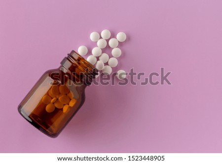 White round tablets scattered around a glass bottle of medicine