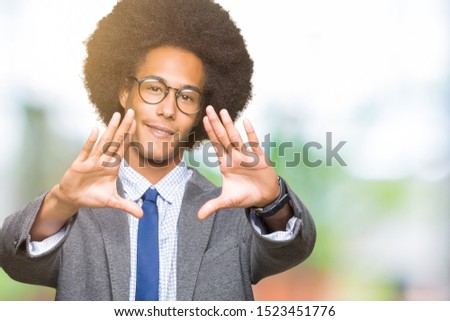 Young african american business man with afro hair wearing glasses Smiling doing frame using hands palms and fingers, camera perspective