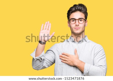 Young handsome man wearing glasses over isolated background Swearing with hand on chest and open palm, making a loyalty promise oath Royalty-Free Stock Photo #1523471876