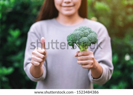 a woman holding and making thumb up to show good sign to a green broccoli 