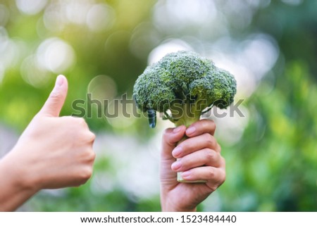 a woman holding and making thumb up to show good sign to a green broccoli 