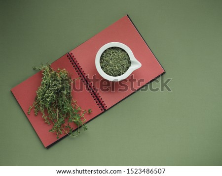Ceramic white bowl of dry thyme (thymus serpyllum) on green and red background. Overhead shot.