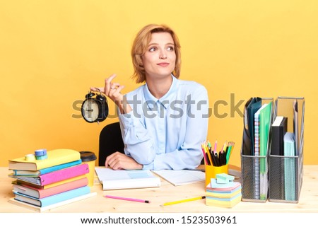 funny dreaming woman holding cloack looking aside, she is waiting for the end of working day, FRiday, weekend, holiday. close up portrait, isolated yellow background