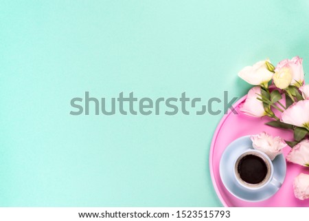 Cup of coffee with bouquet pink eustoma on a rose tray over blue background with copy space, flat lay. Valentines day, birthday, mother or wedding greeting card