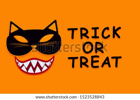 Funny face of cat monster with vampire smile on orange background. Paper decor, photo props with black inscription trick or treat on canvas. Party accessories for celebration happy halloween.