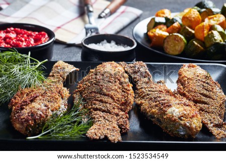 freshly fried crispy crucian carps on a black rectangular plate on a concrete table with fried zucchini and hot tomato sauce, horizontal view from above Royalty-Free Stock Photo #1523534549