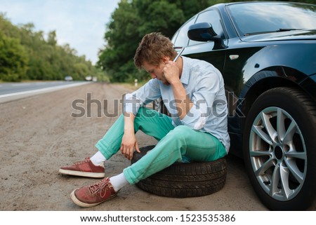 Car breakdown, young man sitting on spare tyre