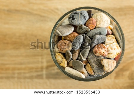 Small sea stones in a glass vessel. The idea of decorating the house with small rocks in a jar on a wooden blurred background. Royalty-Free Stock Photo #1523536433