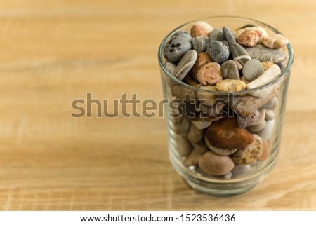 Small sea stones in a glass vessel. The idea of decorating the house with small rocks in a jar on a wooden blurred background. Royalty-Free Stock Photo #1523536436