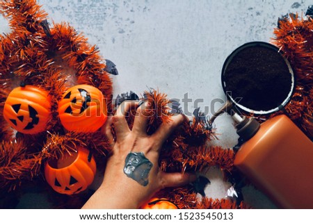 Scary hand with black mud on skin with pumpkin head bucket, brown color cream bottle, coffee ground on plate and Halloween ribbons decorations on marble pattern table