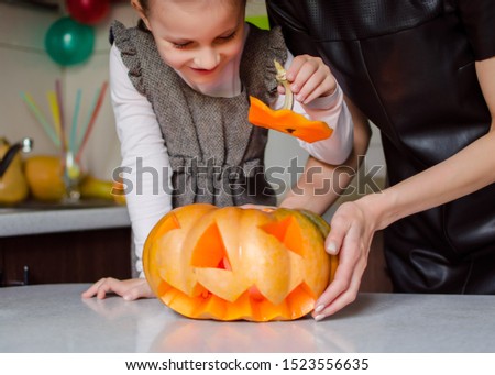 Carved pumpkins into jack-o-lanterns for halloween, decoration and holidays concept.Little girl with mom are carving pumpkin or jack-o-lantern at home. Helloween concept
