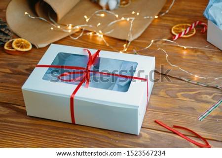 Christmas composition with present box. A Christmas gift box with a red ribbon stands on a wooden table.