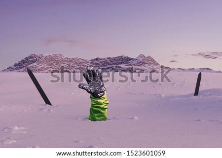 Skier stretching out his snow covered hand next to trekking poles to signal help because of snow avalanche . Danger extreme concept