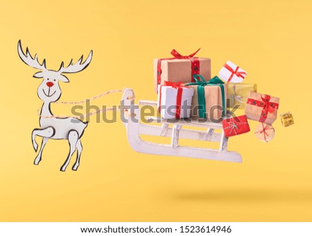 Christmas card conception. Christmas reindeer with sleigh and many gifts in the air isolated on yellow background. Levitation concept.