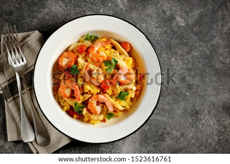 Paella or risotto with chicken breast, shrimp tails, carrots, onions, cherry tomatoes, white wine and chicken stock. Top view. Copy space.