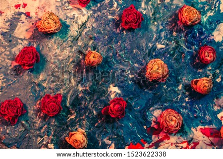 Abstract floral art background. Flat lay arrangement of red and orange dried rose buds on smeared blue paint.