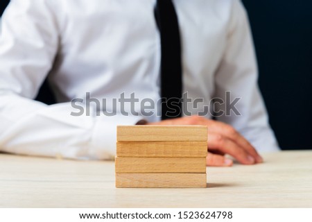 Businessman sitting at his desk with four stacked wooden pegs on it. 