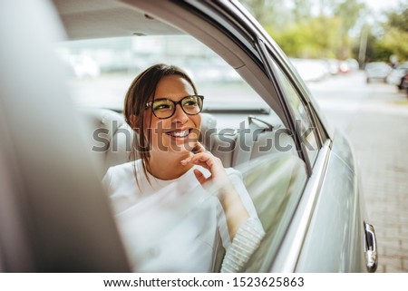 Portrait of a cheerful young woman traveling by a car and looking outside the window.
