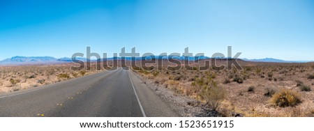 Panoramic View of Open Road in the Desert with Mountains in the Background and Clear Skies