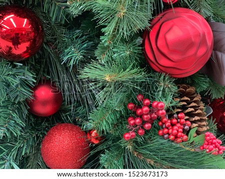 Christmas background green evergreen tree branches decorated with red ornaments and holly berries.