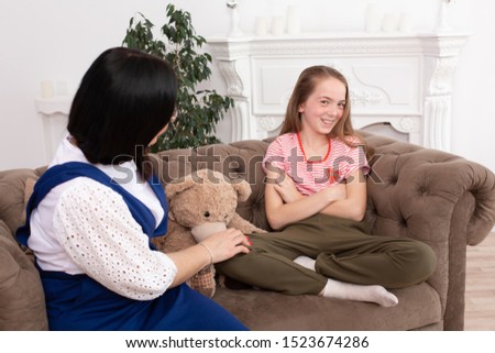 A woman is a professional child psychologist talking with a teenage girl in her cozy office. Psychological assistance to children. Teenager girl shyly smiling.