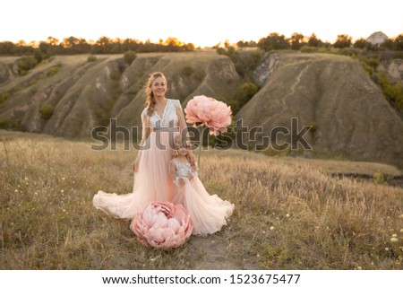 Mom with daughter in pink fairy-tale dresses walk in nature. The childhood of the little princess. Large pink decorative flowers.