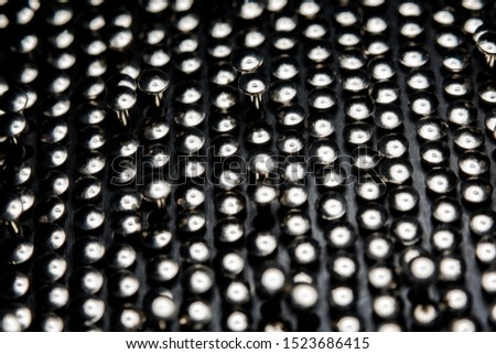 A lot of shiny little nails on a dark background arranged tightly together. Shallow depth of field.