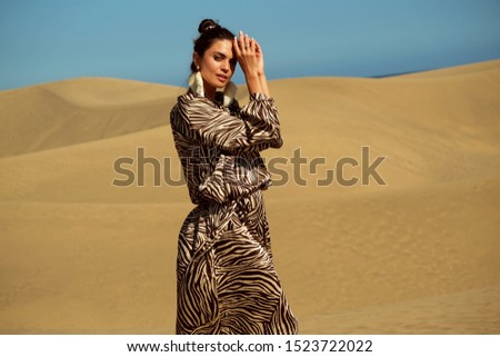 Model wearing animal print dress walking on sandy desert.