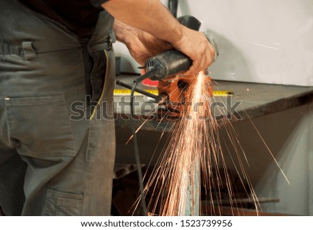 Worker in a workshop grinder processes metal, from which hot bright sparks fly in different directions