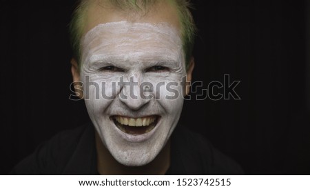 Clown Halloween man portrait. Close-up of an crazy, evil clowns face. White face makeup. Green hair. Scary laugh. Attractive model in Halloween costume. Dark background