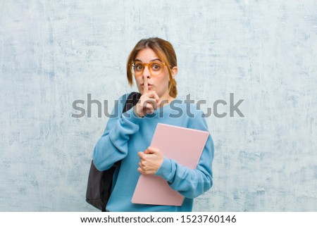 young student woman asking for silence and quiet, gesturing with finger in front of mouth, saying shh or keeping a secret against grunge wall background