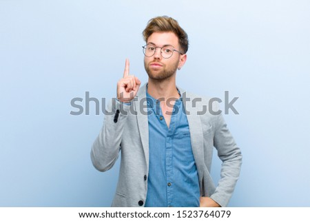 young businessman feeling like a genius holding finger proudly up in the air after realizing a great idea, saying eureka against blue background
