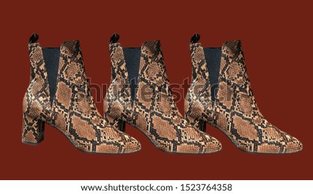 Women's Snakeskin Cowboy Boots isolated on red background. Snake Cowboy Ankle Boots pattern. Close View Of Fashion Casual Female shoes. Brown snake Print Women Boots