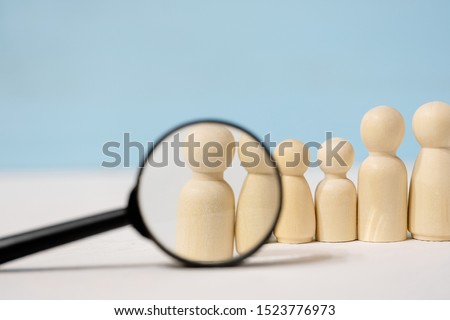 Abstract wooden figures of people under black magnifying glass on blue background. The concept of recruitment. Royalty-Free Stock Photo #1523776973