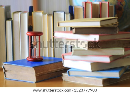 The red hourglass on the table in the library A pile of books in the background selective focus and shallow depth of field